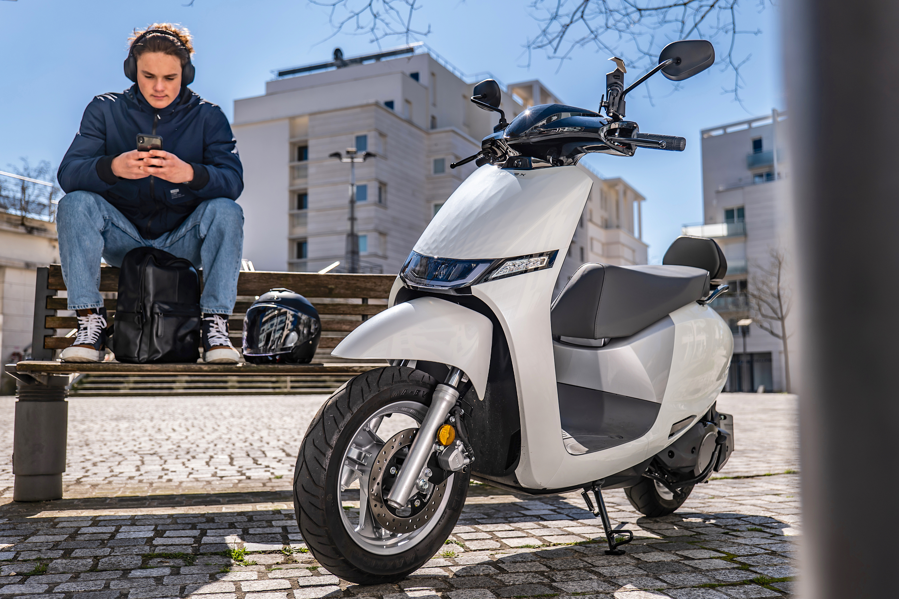 Kymco i-One 2024 : trois quarts avant gauche statique avec adolescent sur un banc
