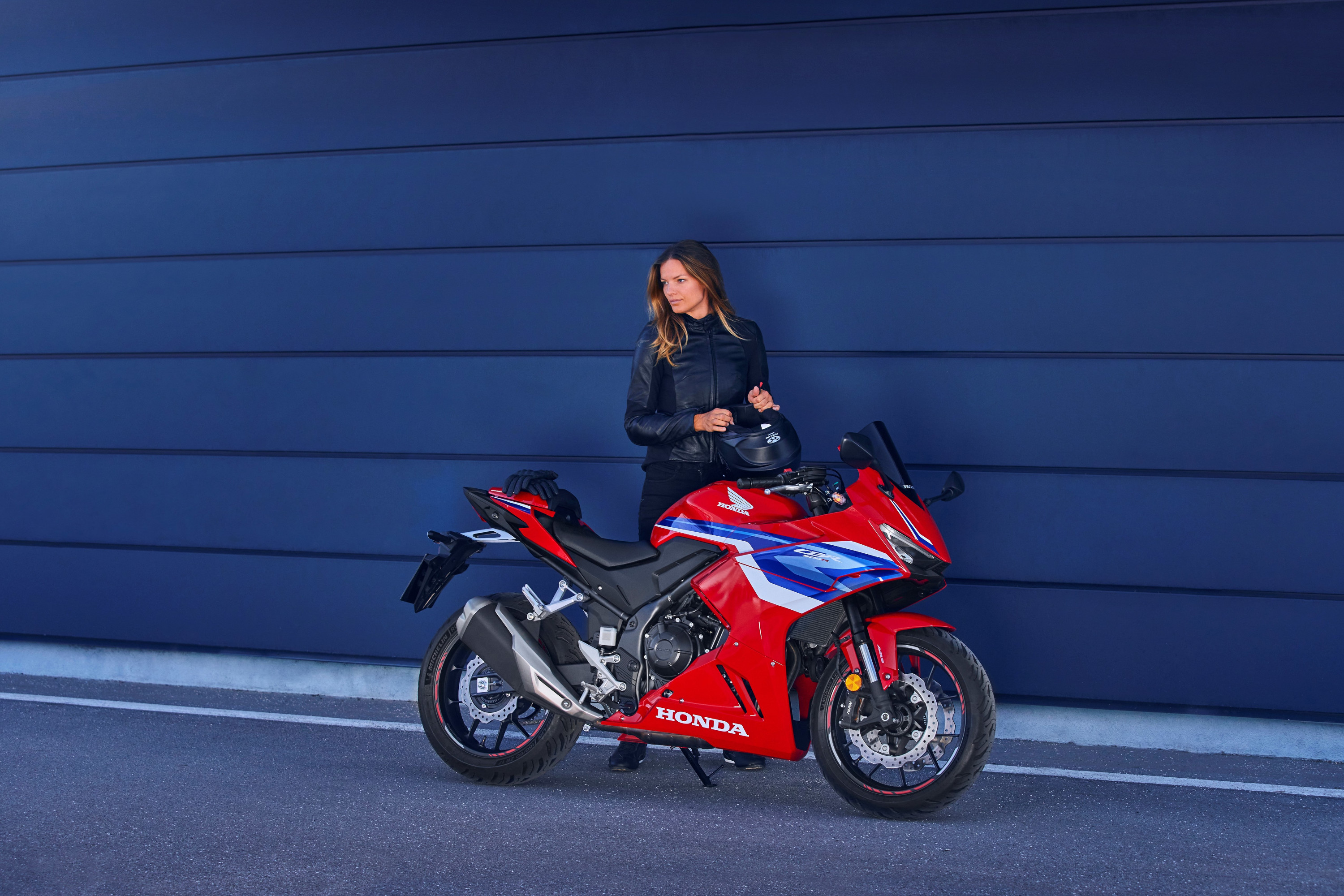 Honda CBR500R 2024 : profil droit devant bâtiment avec jeune femme