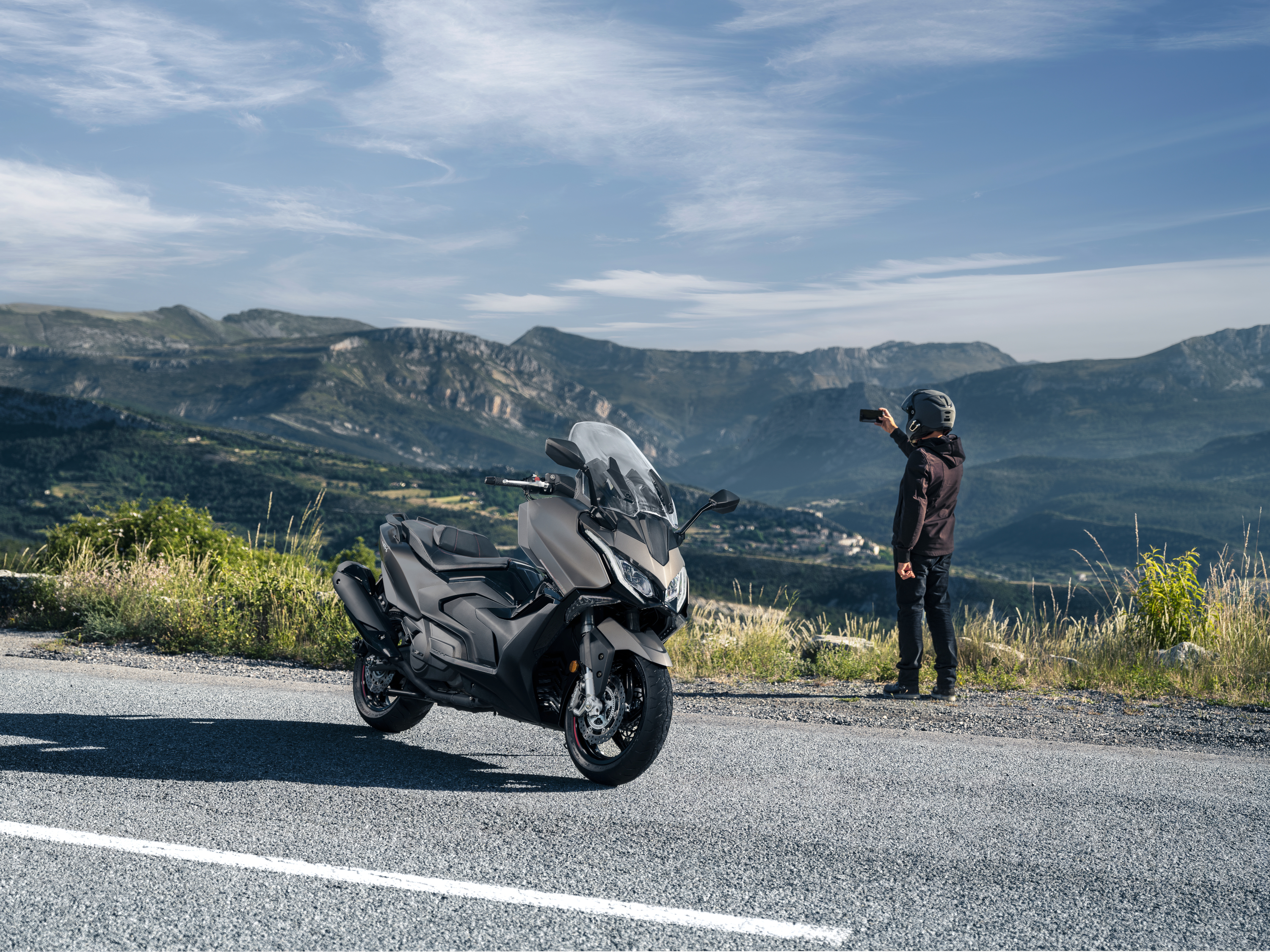 Kymco AK Premium 2024 : trois quarts avant droit avec vue sur montagnes et motard