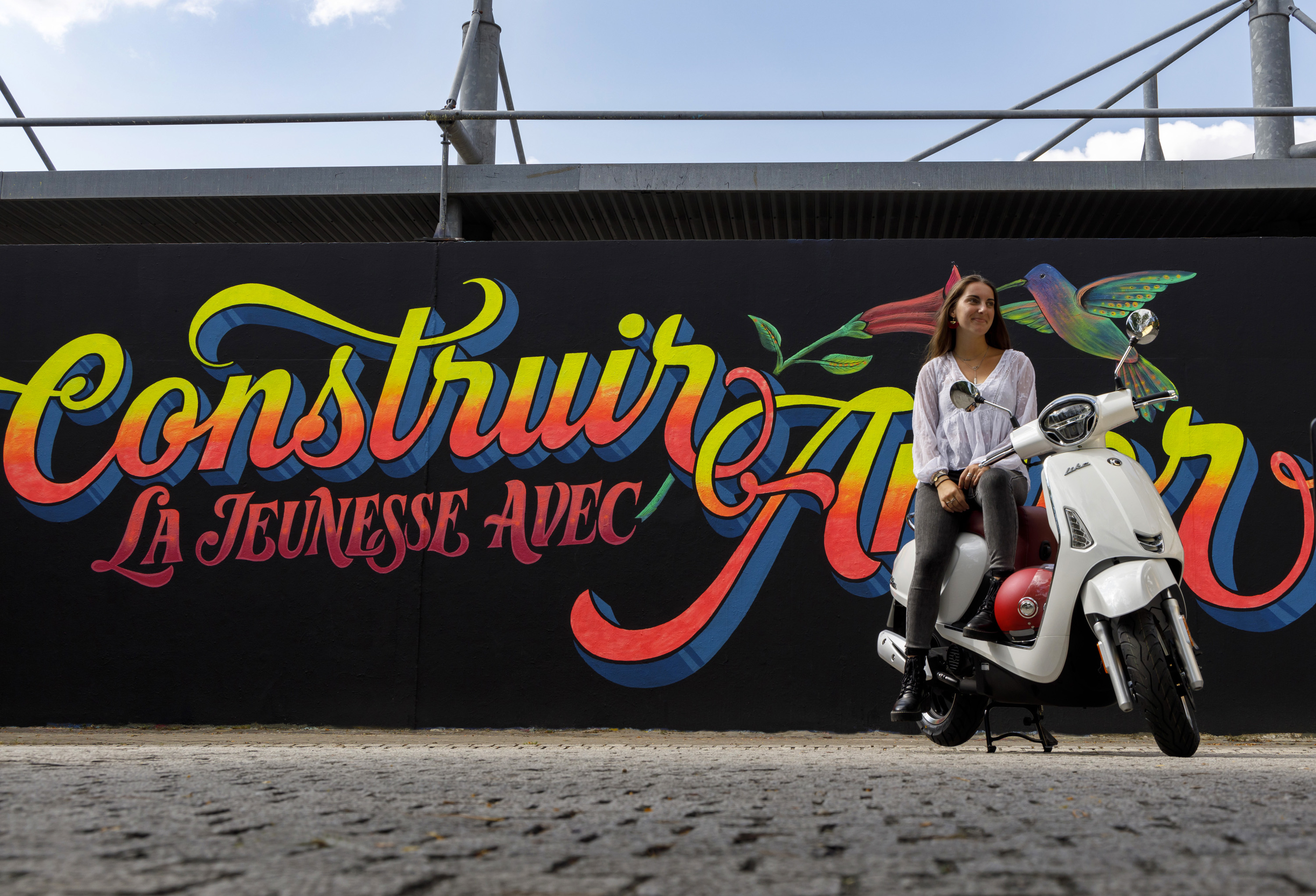 Kymco Like 50 2024 : trois quarts avant droit statique avec jeune femme et street art