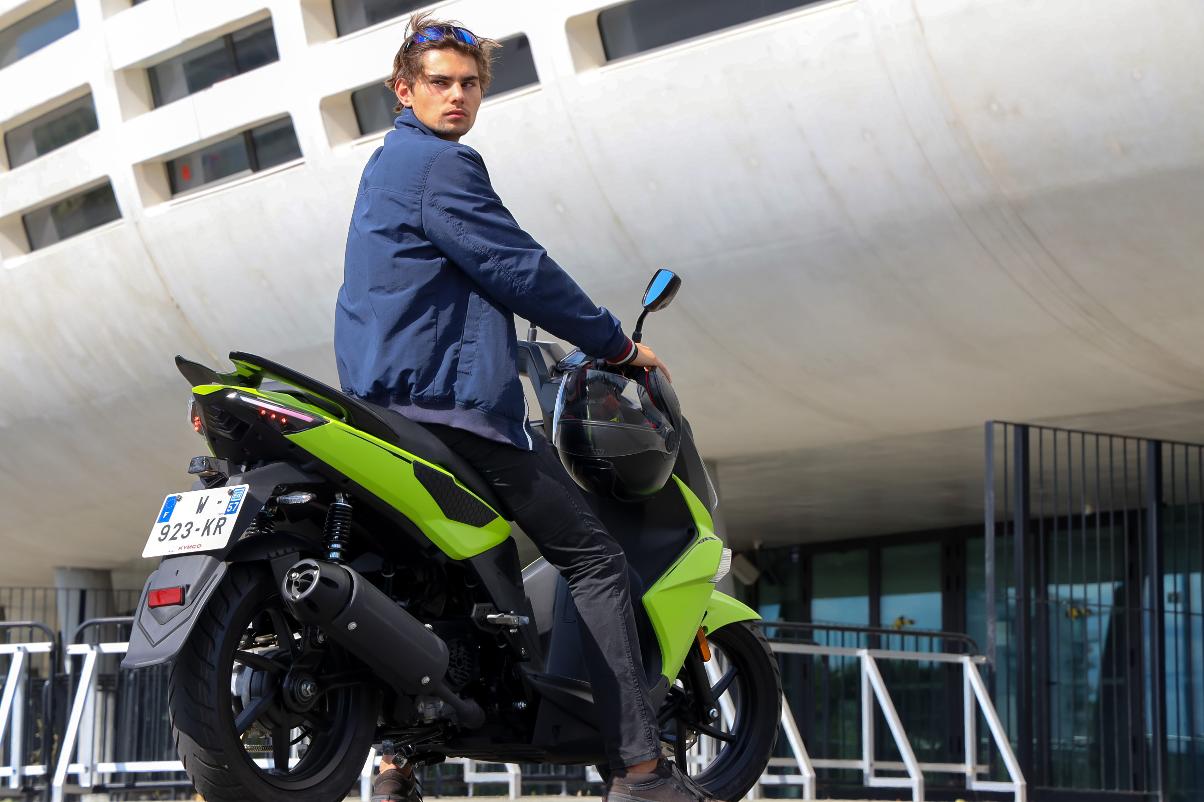 Kymco Super 8 R 2024 : trois quarts arrière droit statique avec jeune homme