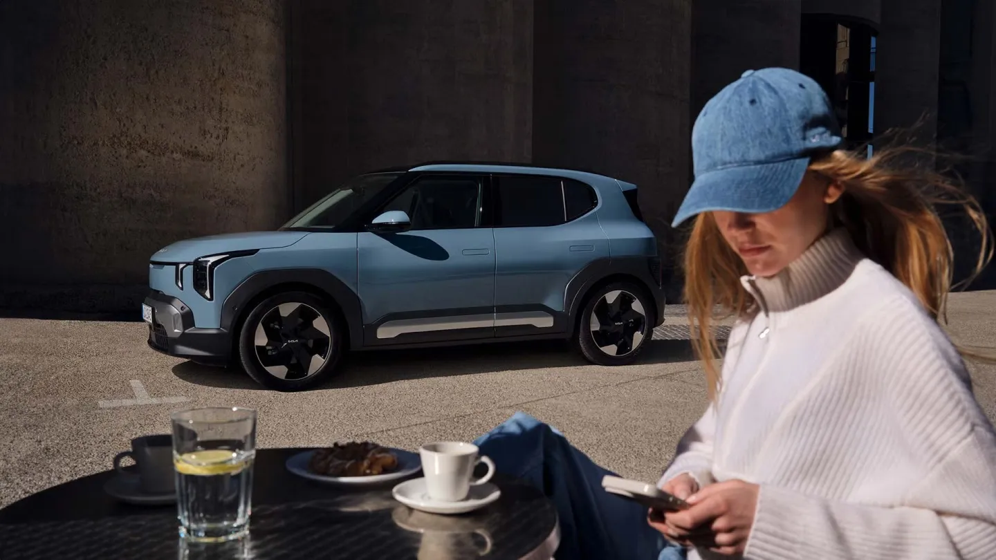 Kia EV2 2026 : profil gauche statique avec modèle en terrasse de café